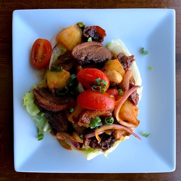 Ddee Thai duck salad with pineapple, tomatoes, red onion, and scallions on a lettuce cup.