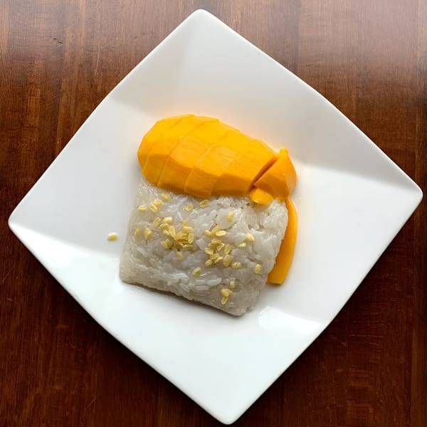 Ddee Thai's mango sticky rice dessert with sliced mango and toasted mung beans on a white plate.