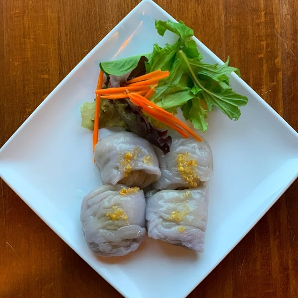 Four Thai dumplings with golden topping, garnished with lettuce and shredded carrots on a white plate.