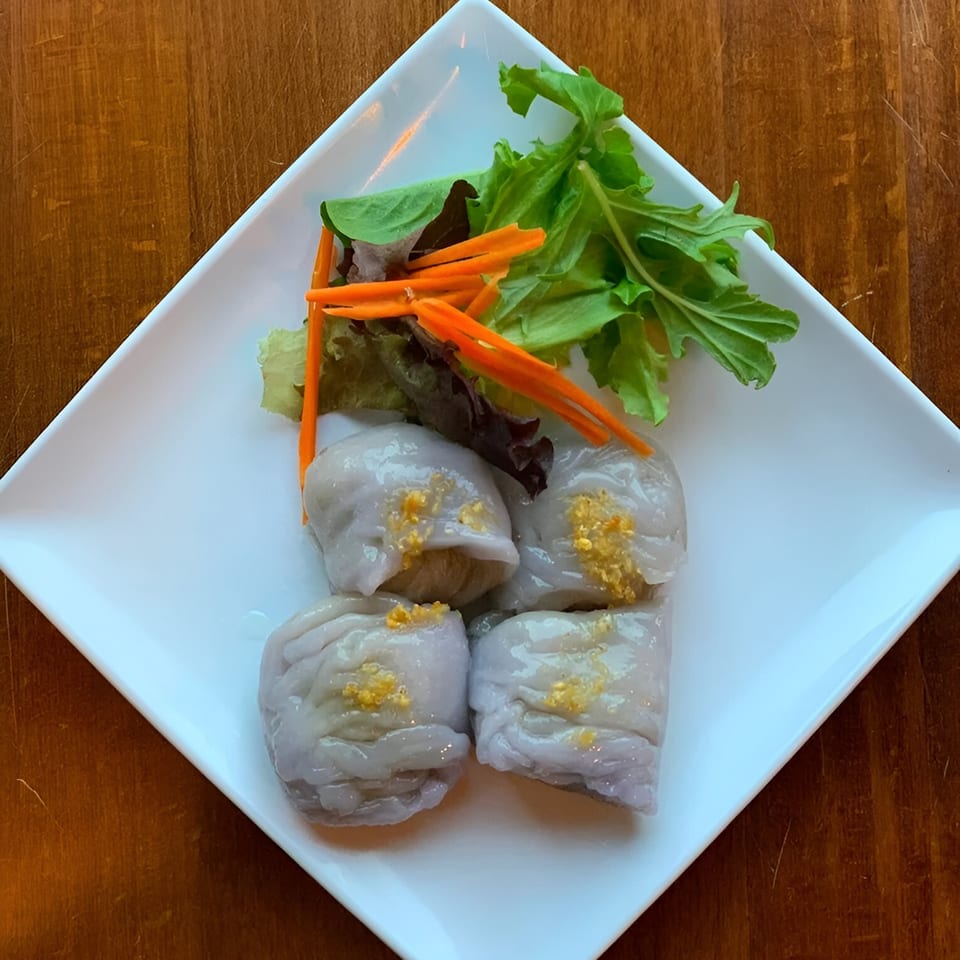 Four Thai dumplings with golden topping, garnished with lettuce and shredded carrots on a white plate.