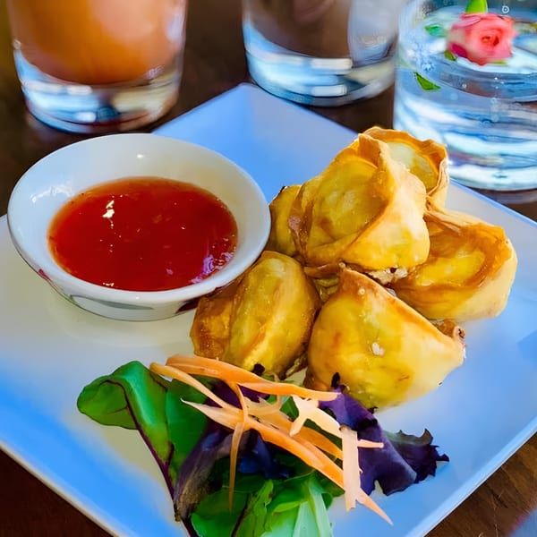 Golden fried Thai dumplings with sweet chili sauce, garnished with lettuce and shredded carrots.
