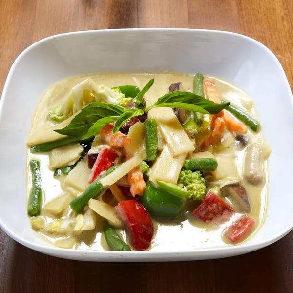 Ddee Thai green curry with bamboo shoots, bell peppers, green beans, and basil in a white bowl.
